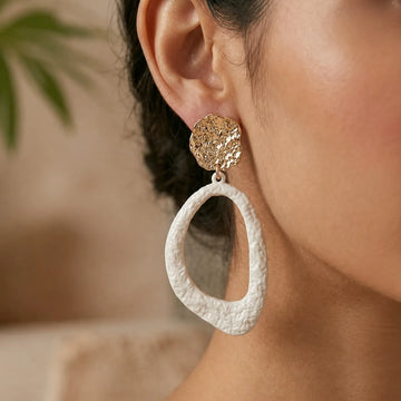 Close-up of a person wearing a gold and white textured earring with a blurred background.
