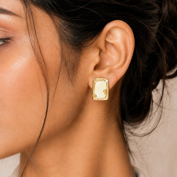 Close-up of a woman's ear wearing a gold earring with a neutral background