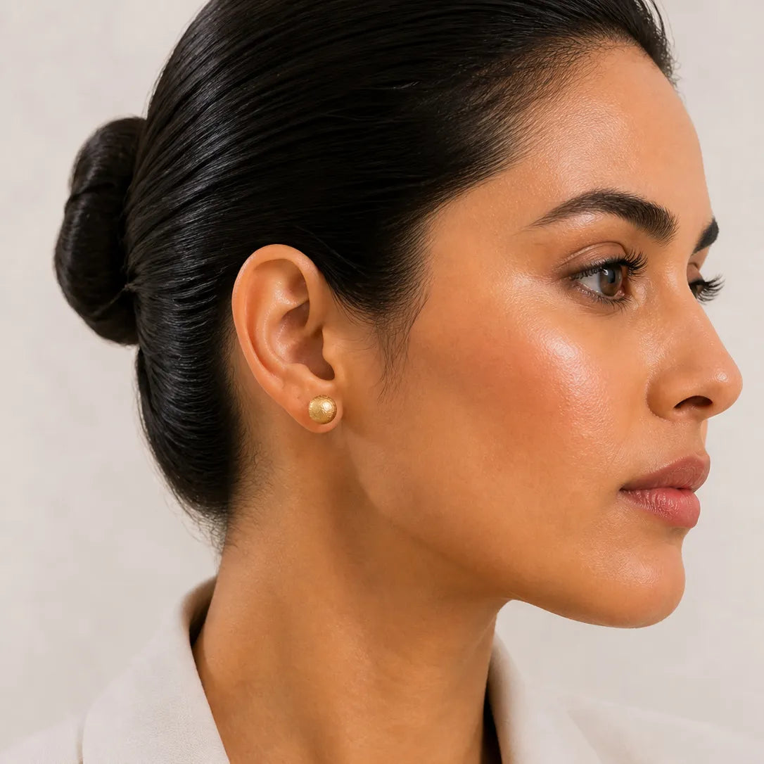 Woman wearing gold earrings with a neutral background