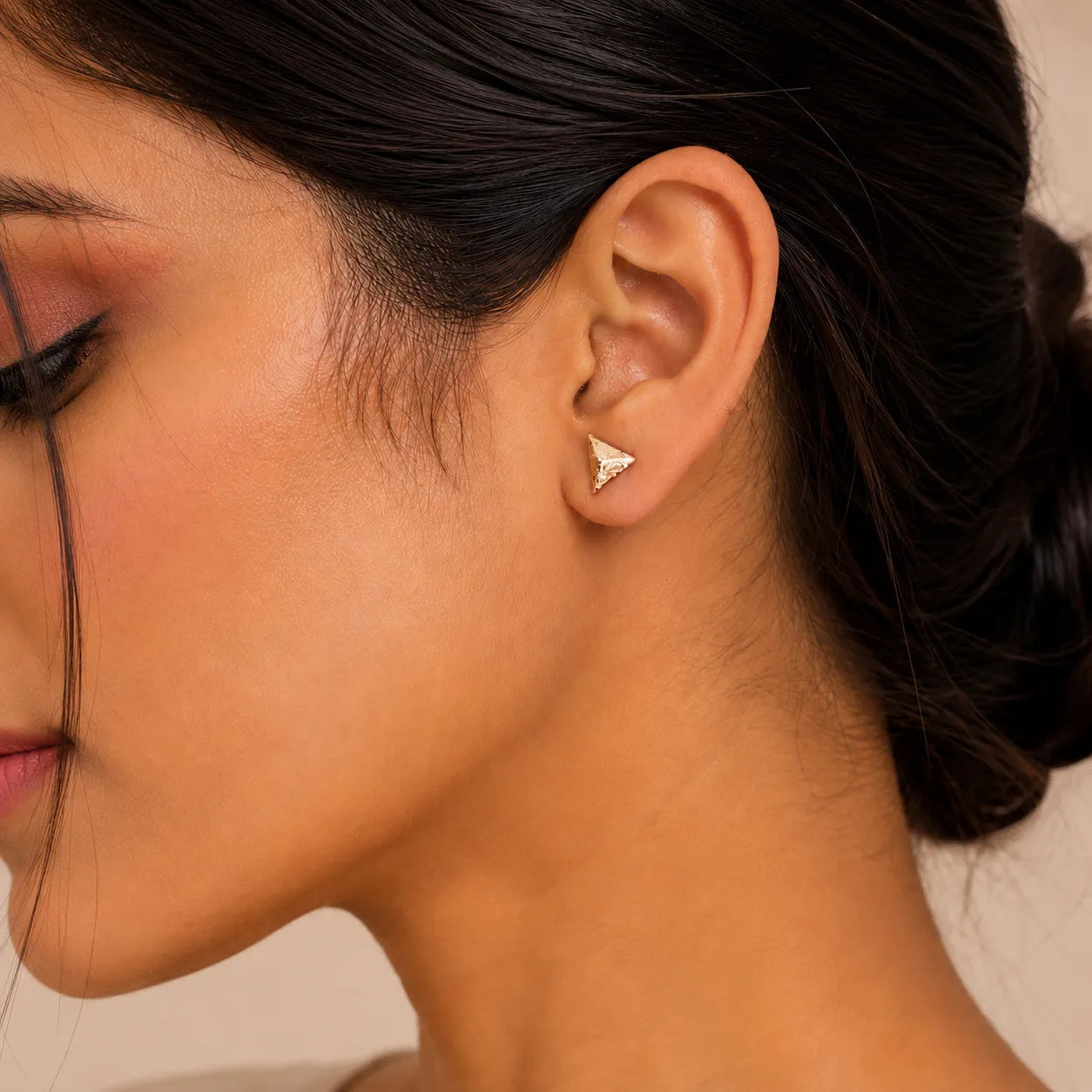 Close-up of a woman wearing a gold triangle earring against a neutral background