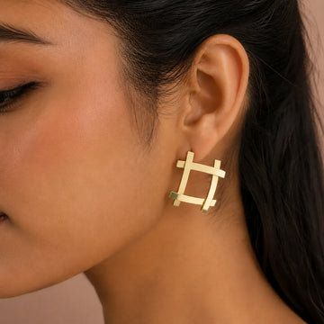 Close-up of a person wearing a gold geometric earring against a neutral background