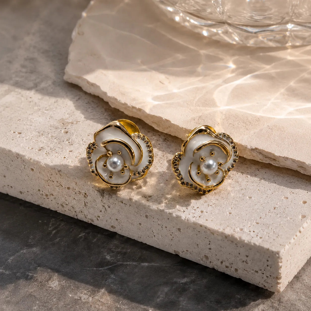 Pair of gold and pearl earrings on a textured stone surface