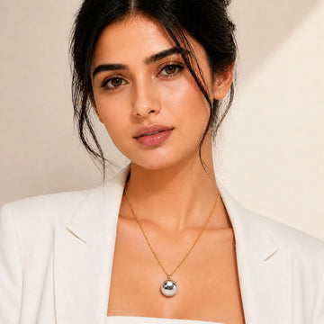 Woman wearing a white blazer and gold necklace with a silver pendant on a neutral background
