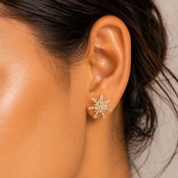 Close-up of an ear wearing a star-shaped gold earring with clear stones.