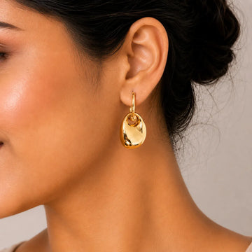 Close-up of a woman wearing a gold earring with a neutral background