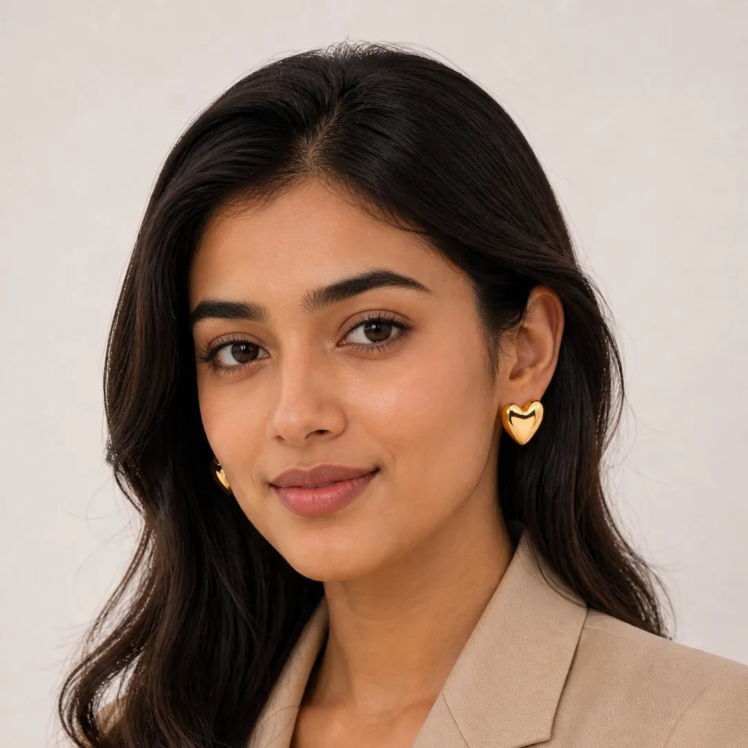 Woman wearing gold heart-shaped earrings against a plain background