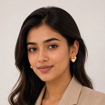 Woman wearing gold heart-shaped earrings against a plain background