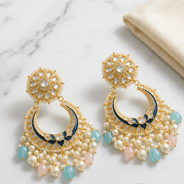 Ornate gold earrings with pearls and blue stones on a marble surface