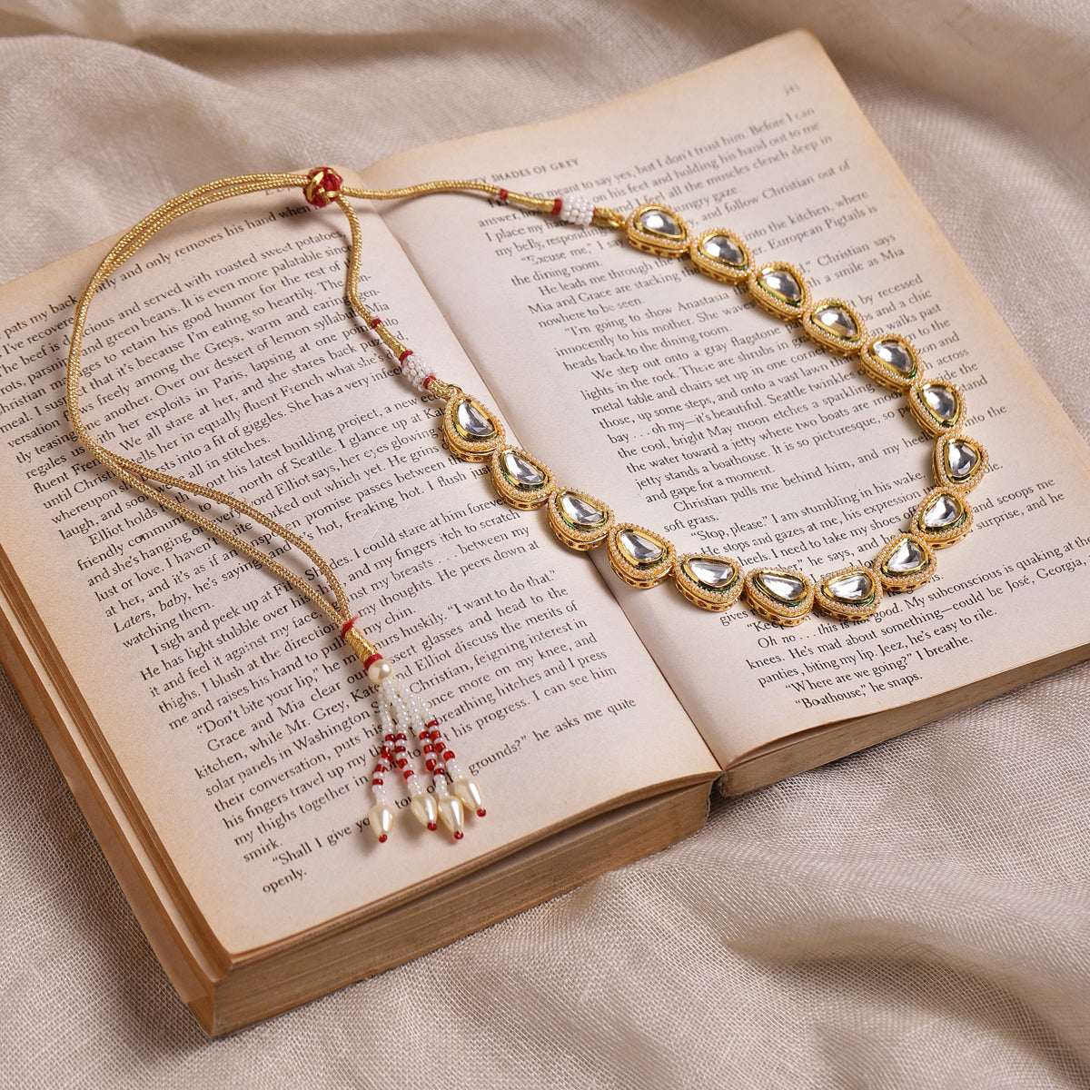 A gold-colored kundan necklace with stone embellishments and red thread details, displayed on an open book.