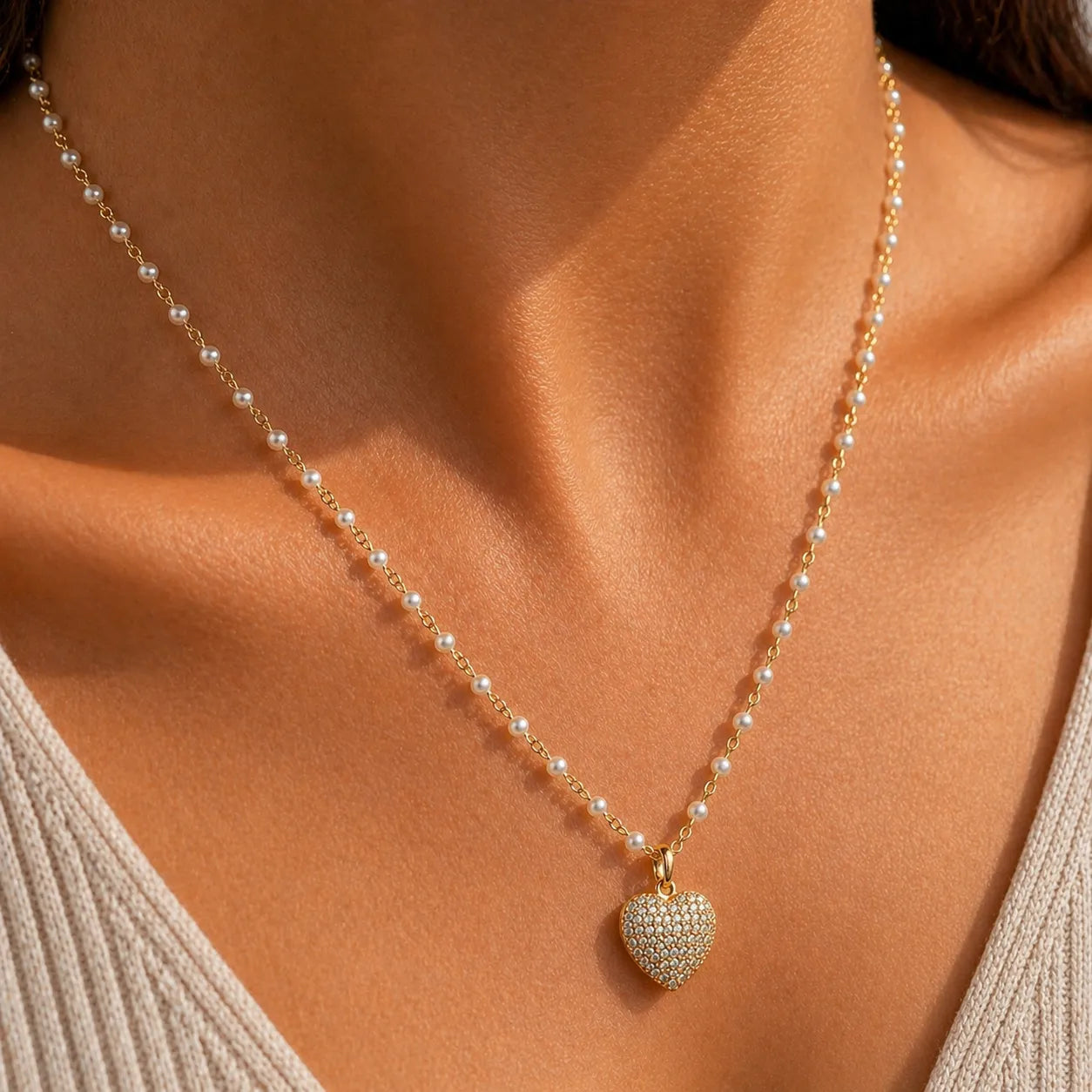 Pearl necklace with a heart-shaped diamond pendant on a person wearing a beige top.