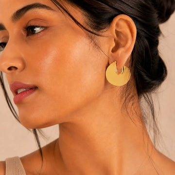 Close-up of a woman wearing gold hoop earrings with a neutral background