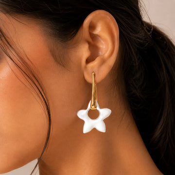 Close-up of a person wearing a gold earring with a white star-shaped pendant.
