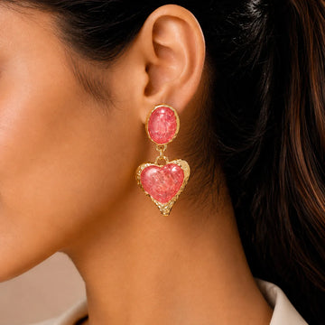 Close-up of a woman wearing pink heart-shaped earrings with gold frames.