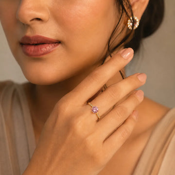 Close-up of a woman wearing a gold ring with a pink gemstone, touching her ear.