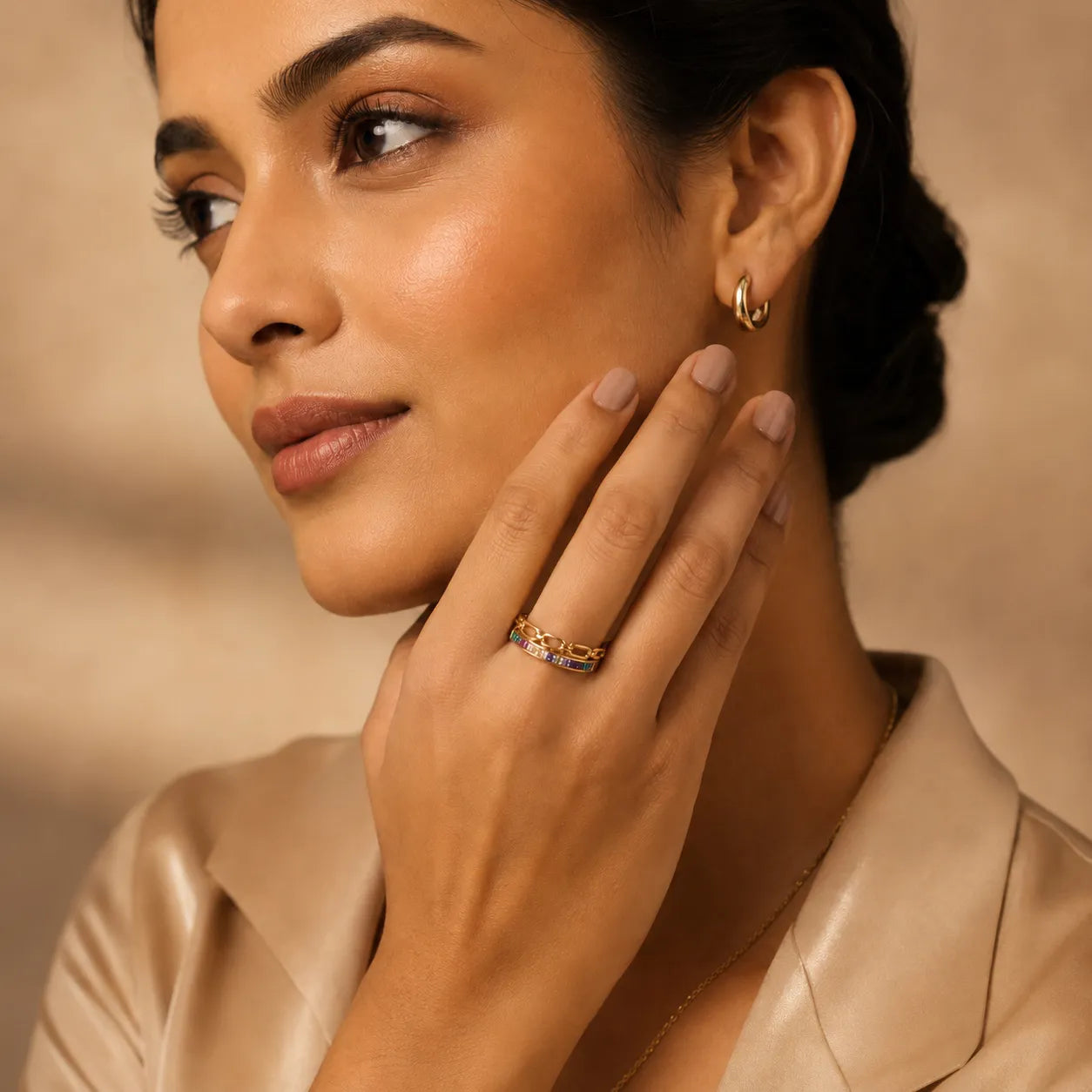 Woman wearing a gold earring and ring against a beige background