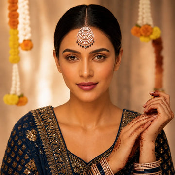 Woman in traditional attire with decorative headpiece and henna on hands against a warm background