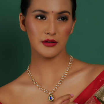 A woman wearing a red saree and a blue and green stone neckpiece with pearls, with a focus on the neckpiece.