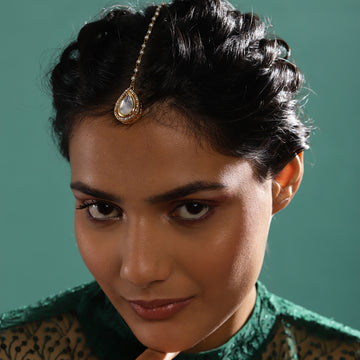 A woman wearing a gold-colored drop kundan maang tikka accessory in her hair.