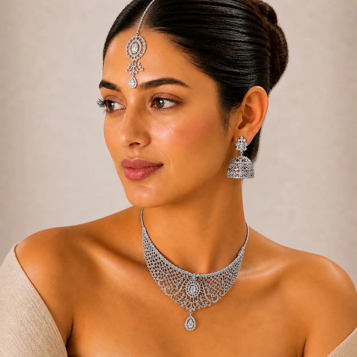 Woman wearing silver jewelry including a necklace, earrings, and a headpiece against a neutral background