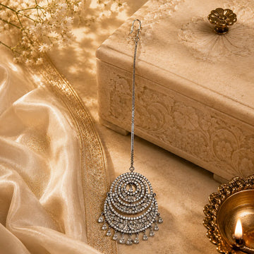 Decorative silver earring on a textured surface with flowers and a box in the background