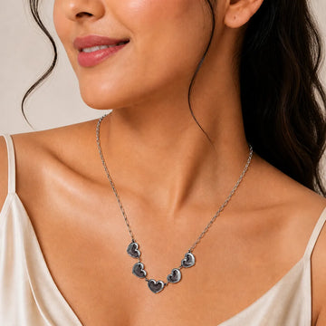 Close-up of a woman wearing a silver necklace with heart pendants on a neutral background