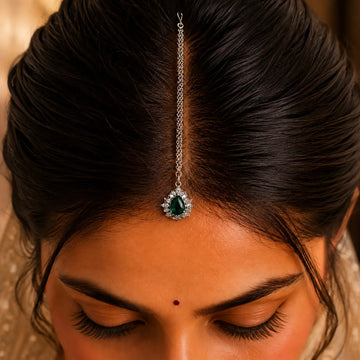 Close-up of a woman's head with a decorative hairpiece featuring a green gemstone.