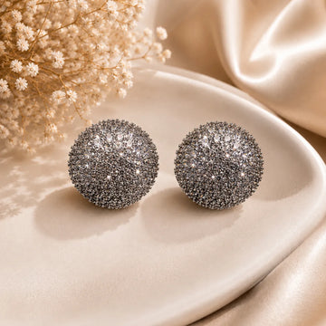 Silver glittery sphere earrings on a beige plate with dried flowers and satin fabric.