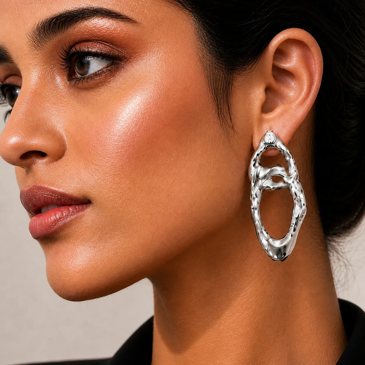 Close-up of a woman wearing a silver hoop earring against a neutral background