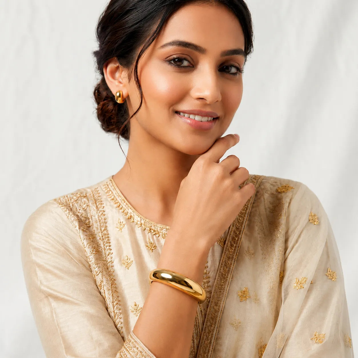 Woman wearing a beige saree with gold embroidery on a white background