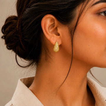 Close-up of a person wearing gold earrings with a neutral background