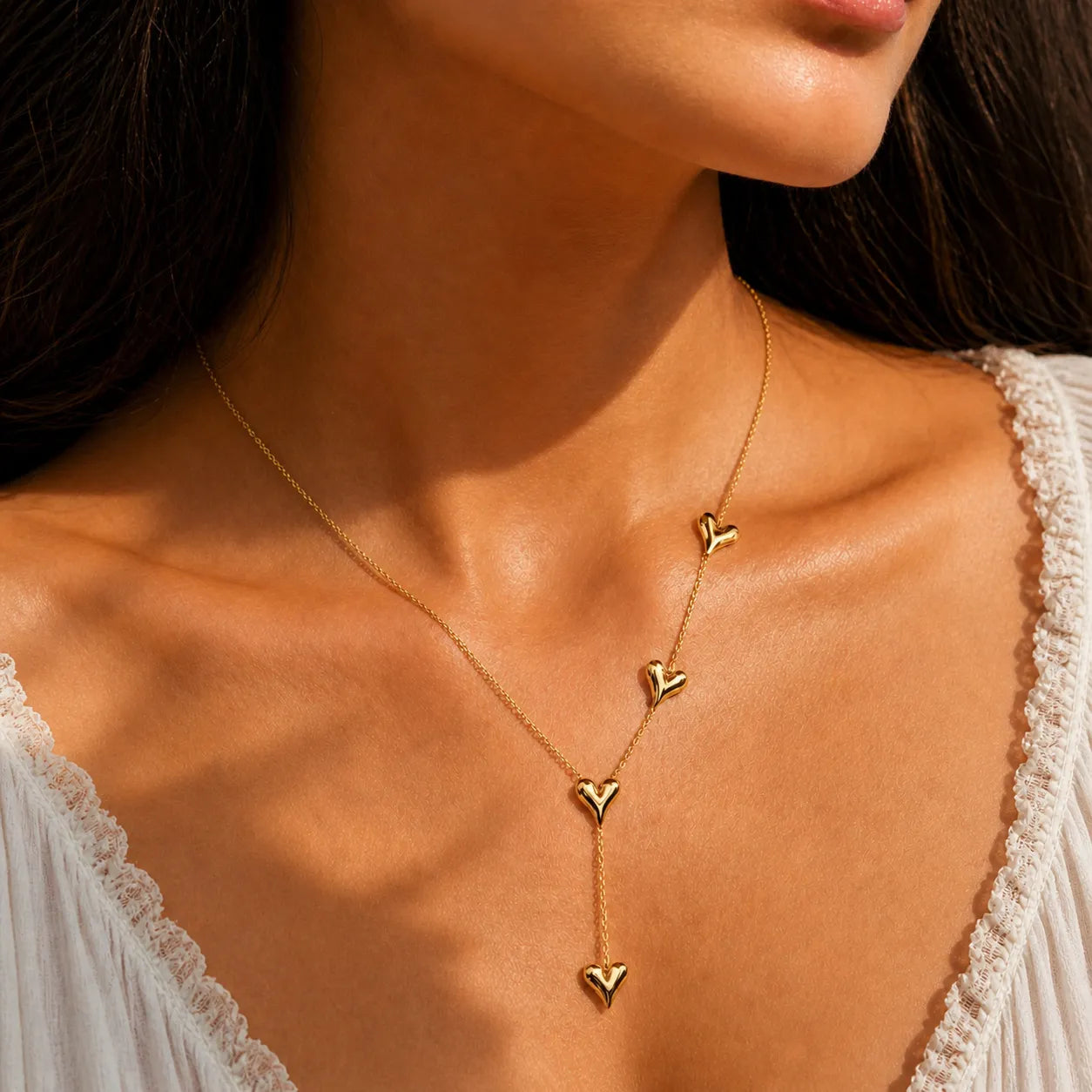 Gold heart-shaped necklace on a person wearing a white lace top.