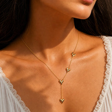 Gold heart-shaped necklace on a person wearing a white lace top.